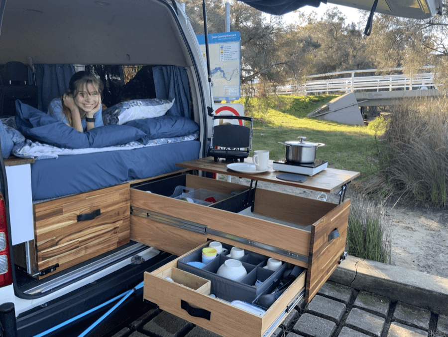 A campervan camp kitchen drawer open at the rear of the vehicle, fitted with cookware and storage