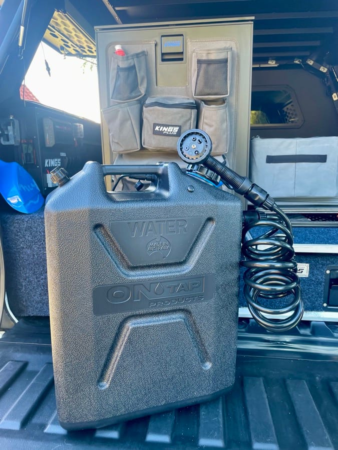 A 22L on-tap water jerry with attached camp shower head set up at the rear of a 4WD canopy